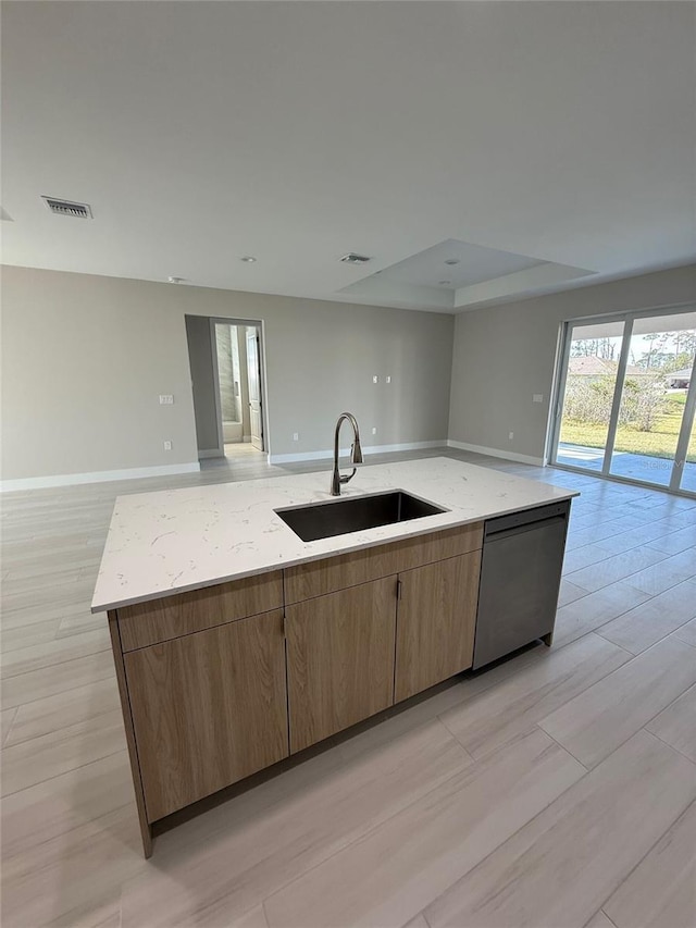 kitchen featuring a kitchen island with sink, sink, light stone counters, and black dishwasher