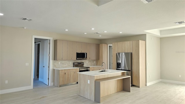 kitchen featuring sink, appliances with stainless steel finishes, light hardwood / wood-style floors, an island with sink, and decorative backsplash