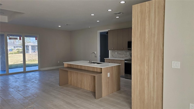 kitchen with sink, tasteful backsplash, light hardwood / wood-style flooring, electric range, and an island with sink