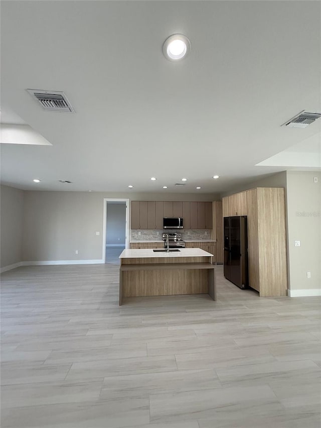 kitchen with tasteful backsplash, a kitchen island with sink, sink, and black refrigerator with ice dispenser