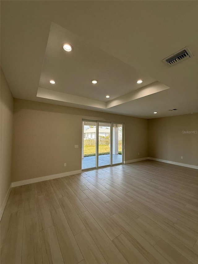 spare room featuring a tray ceiling and light hardwood / wood-style floors