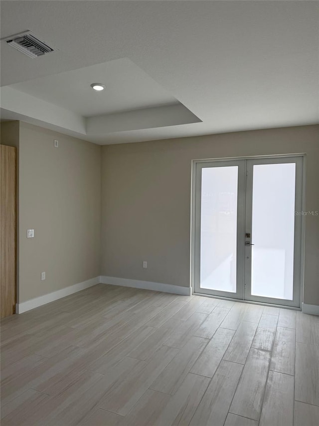 spare room with french doors, a tray ceiling, and light hardwood / wood-style floors