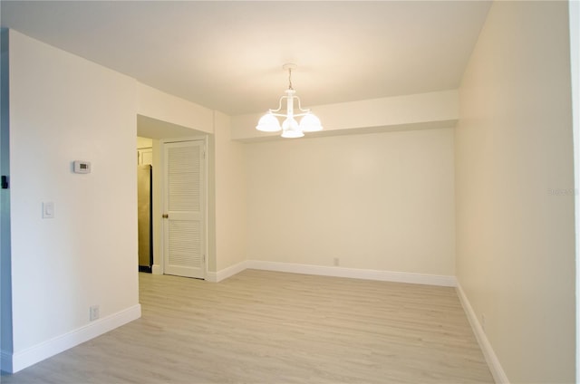 spare room with an inviting chandelier and light hardwood / wood-style floors