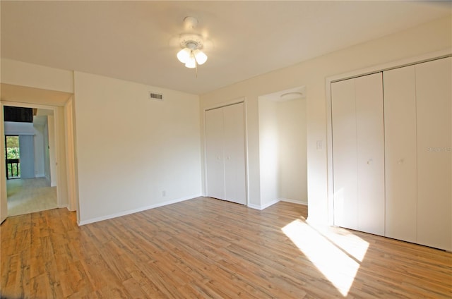 unfurnished bedroom with multiple closets, ceiling fan, and light wood-type flooring