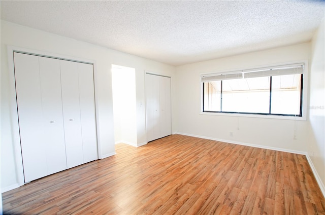 unfurnished bedroom featuring a textured ceiling, light hardwood / wood-style floors, and multiple closets