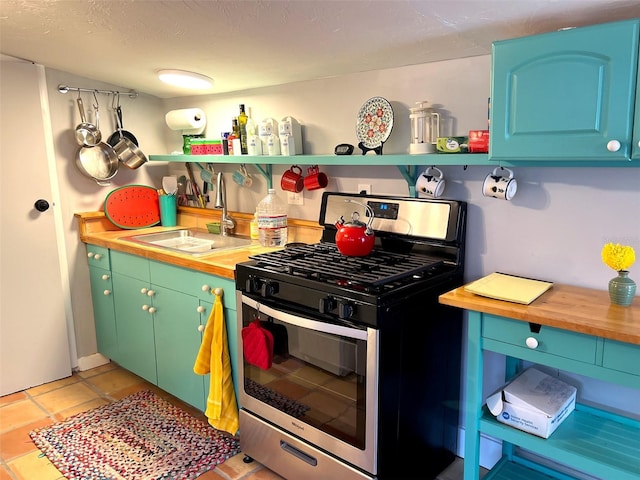 kitchen with wooden counters, stainless steel range with gas stovetop, sink, and light tile patterned floors