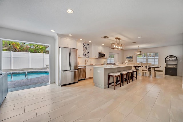 kitchen with a kitchen island, appliances with stainless steel finishes, decorative light fixtures, white cabinetry, and a breakfast bar area