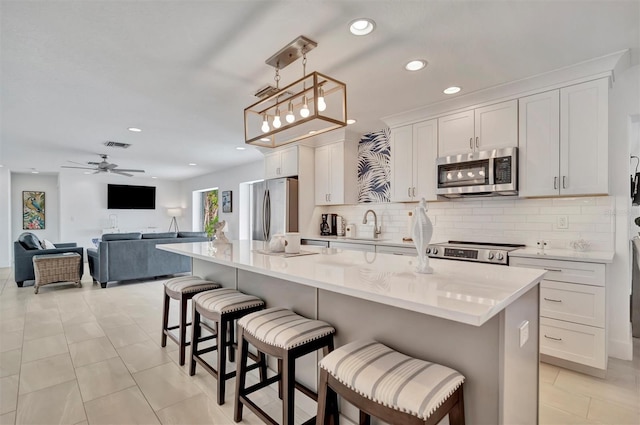 kitchen with a kitchen island with sink, decorative light fixtures, white cabinets, and appliances with stainless steel finishes