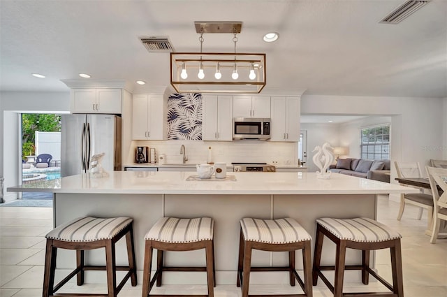 kitchen with a breakfast bar, white cabinetry, appliances with stainless steel finishes, pendant lighting, and a large island