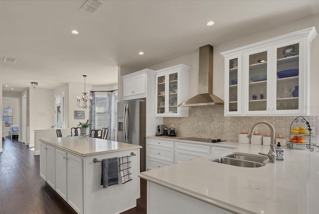 kitchen with pendant lighting, wall chimney range hood, sink, stainless steel refrigerator with ice dispenser, and white cabinets