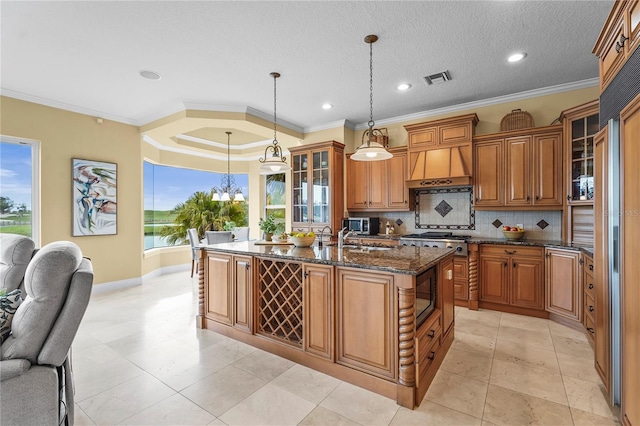 kitchen with a kitchen island with sink, brown cabinets, glass insert cabinets, and decorative light fixtures