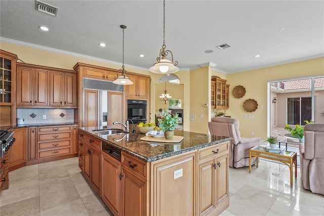 kitchen with pendant lighting, visible vents, glass insert cabinets, a sink, and an island with sink