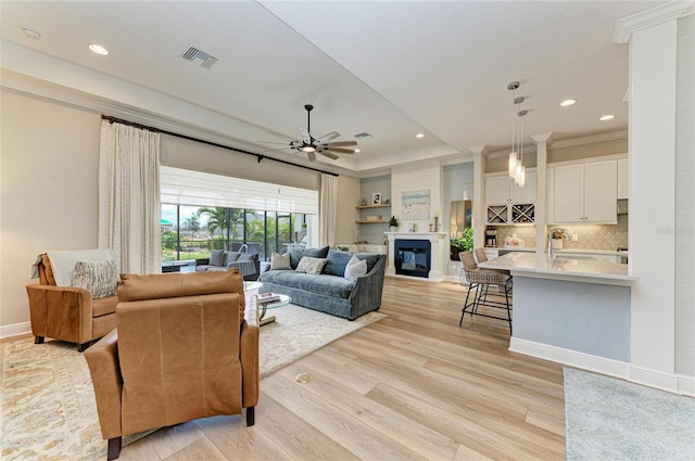 living room with ceiling fan, a tray ceiling, sink, and light wood-type flooring