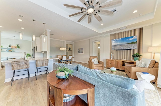 living room featuring crown molding, a tray ceiling, ceiling fan, and light hardwood / wood-style flooring