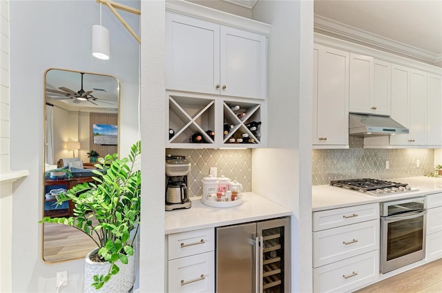 bar with hanging light fixtures, backsplash, stainless steel appliances, white cabinets, and beverage cooler