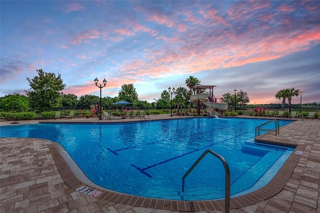 pool at dusk with a water slide and a patio area