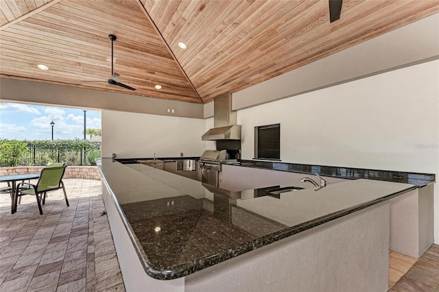 kitchen featuring dark stone countertops, hanging light fixtures, wood ceiling, and wall chimney exhaust hood