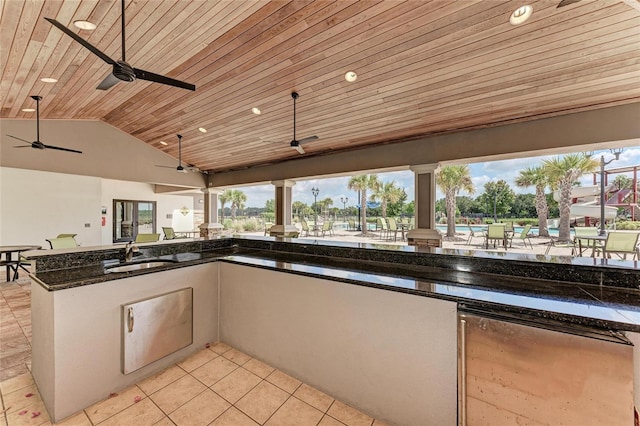 kitchen with sink, wood ceiling, light tile patterned floors, vaulted ceiling, and dark stone counters