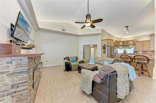 living room featuring ceiling fan, lofted ceiling, a stone fireplace, and light hardwood / wood-style floors