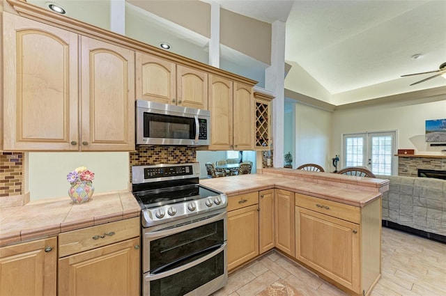 kitchen featuring lofted ceiling, stainless steel appliances, tile counters, kitchen peninsula, and light brown cabinets