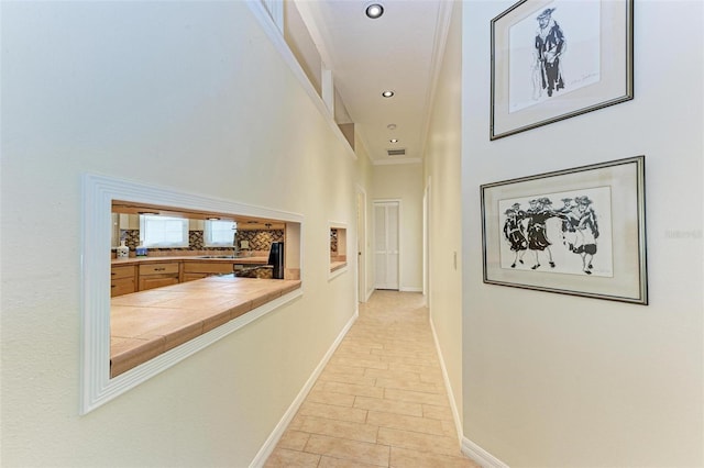 corridor with a high ceiling, crown molding, and light tile patterned flooring