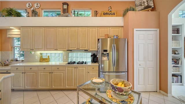 kitchen with light tile patterned floors, stainless steel fridge, backsplash, black gas stovetop, and light brown cabinets