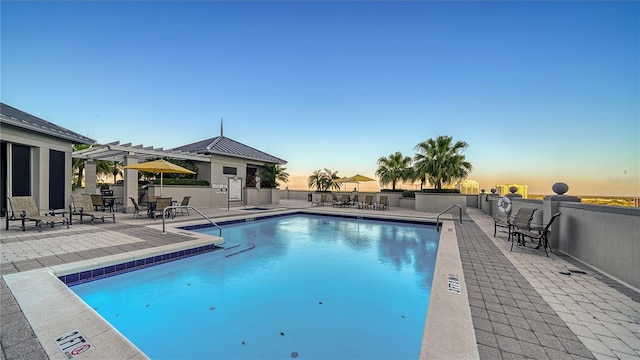 pool at dusk featuring a pergola and a patio