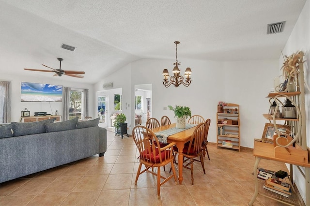 dining space with ceiling fan with notable chandelier, lofted ceiling, light tile patterned floors, and a textured ceiling