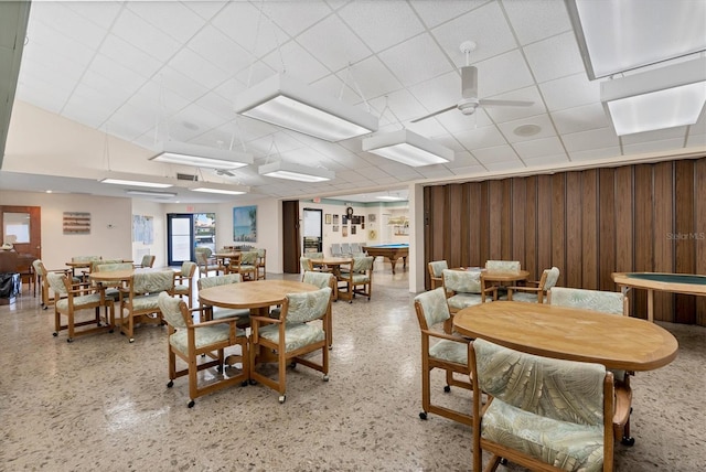 dining room with ceiling fan, a paneled ceiling, and wooden walls