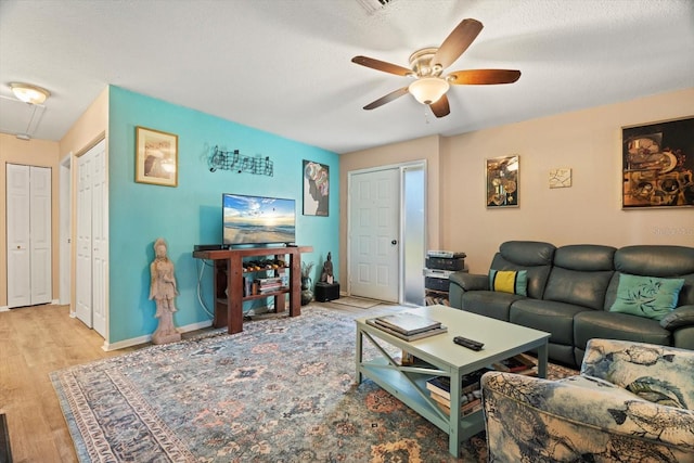 living room with ceiling fan, a textured ceiling, and light wood-type flooring