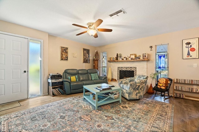 living room featuring hardwood / wood-style flooring, a brick fireplace, a textured ceiling, and ceiling fan