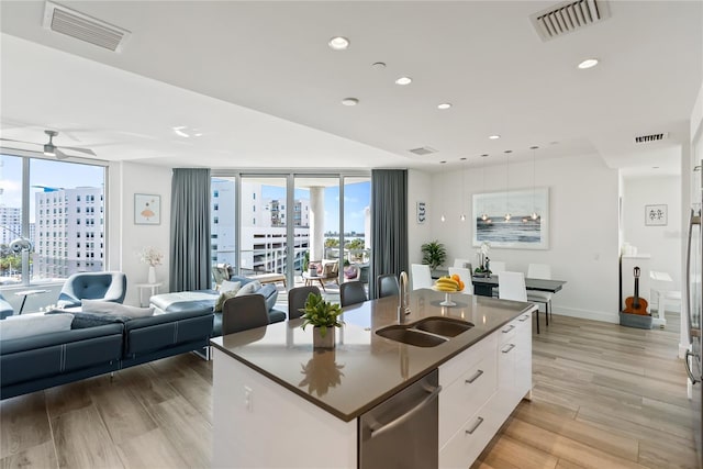 kitchen with sink, light hardwood / wood-style floors, an island with sink, white cabinets, and stainless steel dishwasher