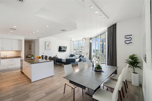 dining area featuring ceiling fan, sink, a wall of windows, and light hardwood / wood-style flooring