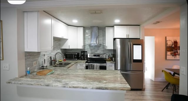 kitchen with sink, white cabinets, light stone counters, stainless steel appliances, and wall chimney exhaust hood