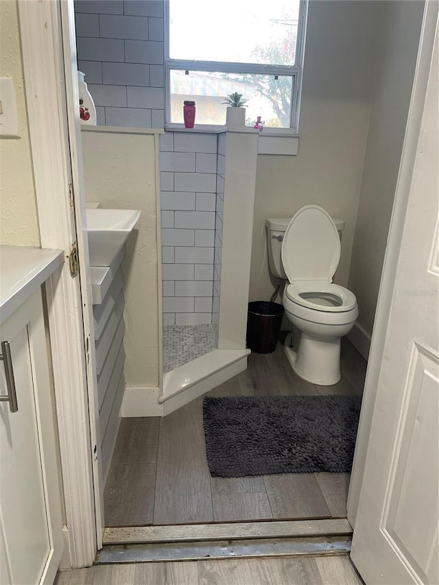 bathroom with vanity, toilet, hardwood / wood-style floors, and a tile shower