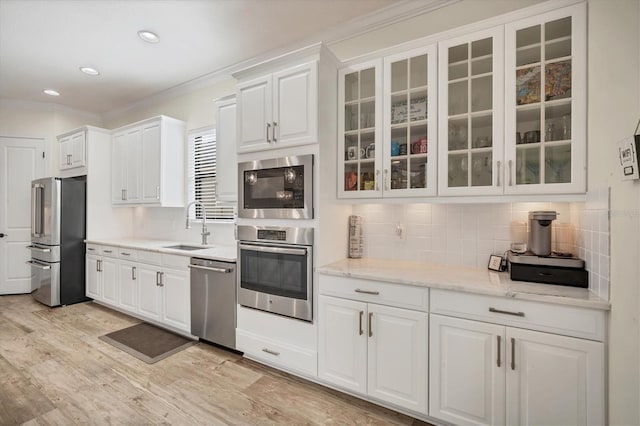 kitchen with sink, white cabinetry, light wood-type flooring, appliances with stainless steel finishes, and backsplash