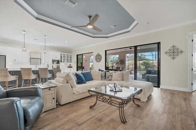 living room featuring crown molding, ceiling fan, a raised ceiling, and light hardwood / wood-style flooring