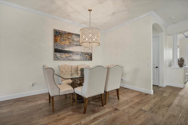 dining area featuring crown molding, wood-type flooring, an inviting chandelier, and ornate columns