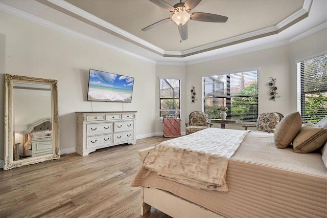 bedroom featuring multiple windows, light hardwood / wood-style flooring, ornamental molding, and a raised ceiling