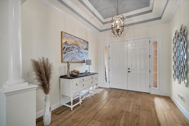 foyer entrance with a raised ceiling, wood-type flooring, ornamental molding, and an inviting chandelier