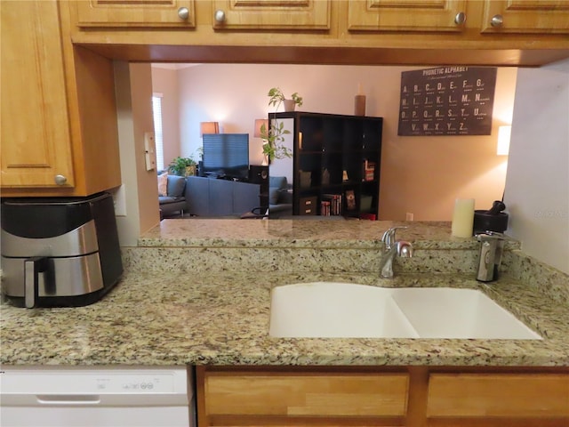 kitchen featuring light stone counters, white dishwasher, and sink