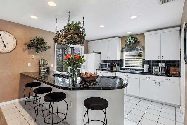 kitchen featuring light tile patterned flooring, white cabinetry, a kitchen bar, white fridge with ice dispenser, and kitchen peninsula