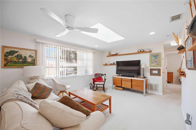 living room featuring light carpet, ceiling fan, and a skylight