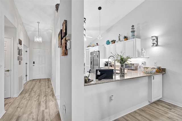 kitchen featuring stone counters, white cabinets, stainless steel fridge, hanging light fixtures, and light hardwood / wood-style flooring