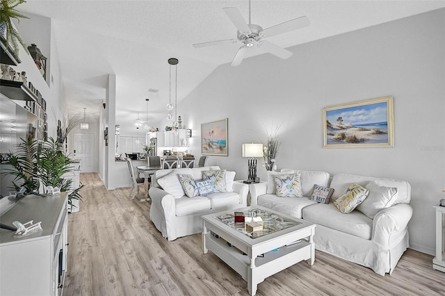 living room with ceiling fan, high vaulted ceiling, a textured ceiling, and light hardwood / wood-style floors