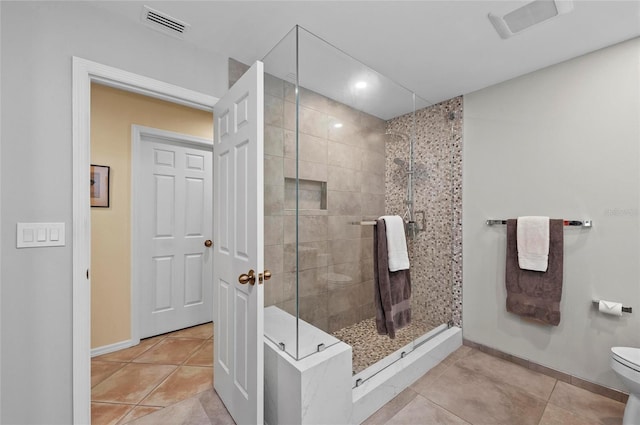 bathroom featuring tiled shower, toilet, and tile patterned flooring