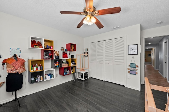 recreation room featuring ceiling fan, dark wood-type flooring, and a textured ceiling