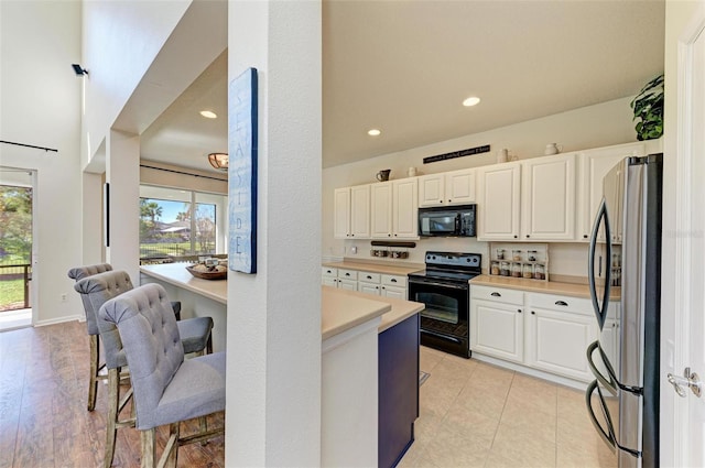 kitchen with white cabinets, light tile patterned floors, and black appliances