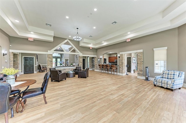 interior space featuring a notable chandelier, a towering ceiling, light hardwood / wood-style flooring, and decorative columns