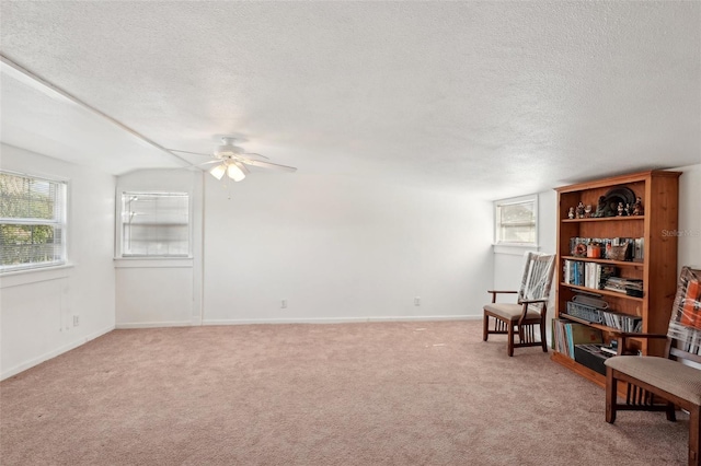 sitting room with ceiling fan, vaulted ceiling, light carpet, and a textured ceiling